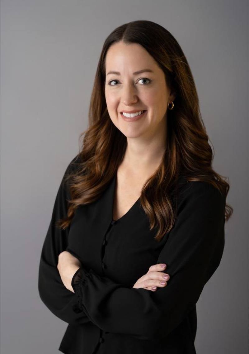Dr. Kasey Gentilin stands with her arms crossed. She wears a black blouse against a gray background.