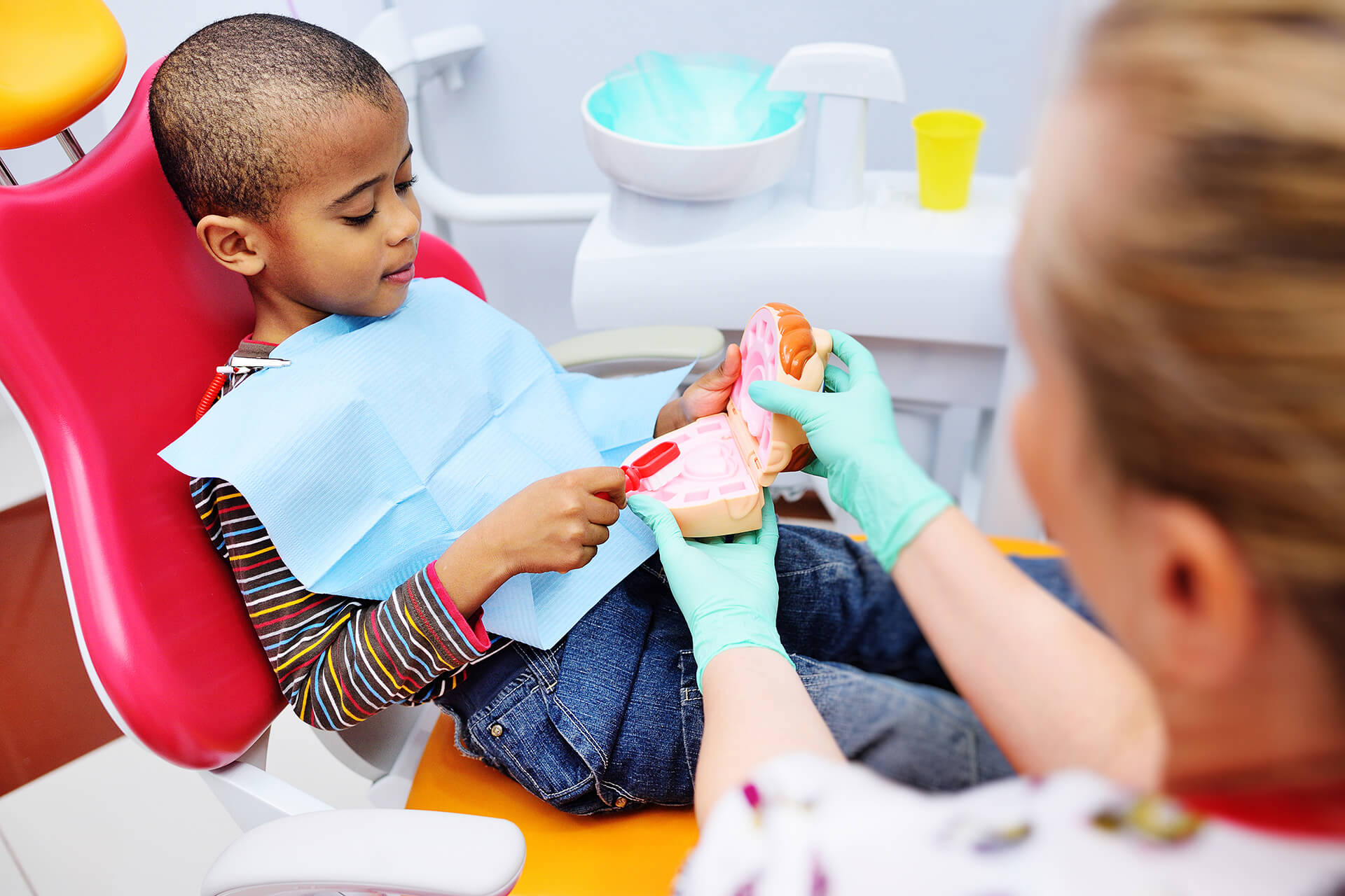 A pediatric dentist teaches an African American child how to brush his teeth properly.